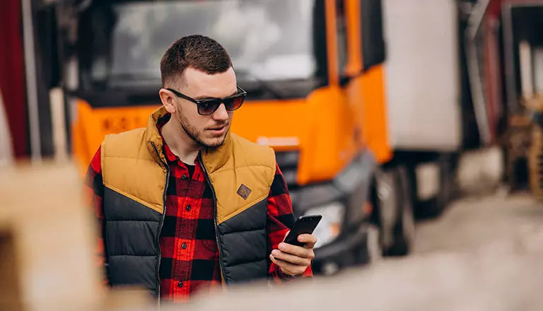 Hombre usando un celular con un camión de fondo
